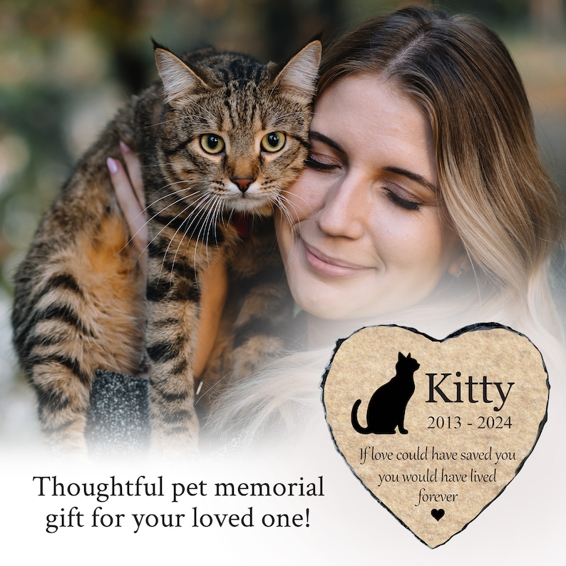 May include: A person holds a tabby cat, with a heart-shaped memorial stone in the foreground. The stone features a black cat silhouette, the name "Kitty", dates 2013-2024, and the inscription "If love could have saved you you would have lived forever."
