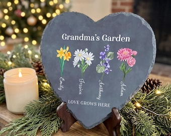 May include: A heart-shaped slate plaque featuring the text Grandma's Garden at the top and LOVE GROWS HERE at the bottom. Four floral illustrations are printed in the center, each labeled with the names Emily, Jessica, Anthony, and Adam.