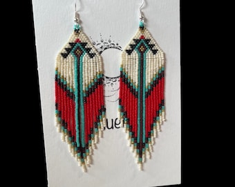 Op de afbeelding: Een paar lange, geperde oorbellen met een geometrisch patroon in rood, wit, zwart en turquoise. De oorbellen hangen aan zilveren haakjes.