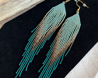 Op de afbeelding: Lange, geperde oorbellen met een gradiënt van turquoise, goud en lichtgroen. De oorbellen zijn gemaakt van kleine kralen en hebben een delicate, bohemian stijl.