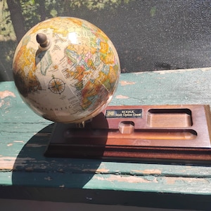 May include: A vintage globe with a cream-coloured surface, displaying a detailed map of the world. The globe sits on a wooden base with a small rectangular slot and the text "KODAK Stock Option Grant". The globe is approximately 20 cm tall.