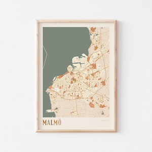 May include: Framed print of a map of Malmö, Sweden, in muted tones of beige, rust, and olive green. The city map is detailed, showing streets and buildings. The word "MALMÖ" is printed at the bottom in a matching color scheme.