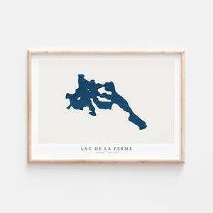 Puede incluir: Una impresión enmarcada con un mapa minimalista del Lac de la Ferme, Quebec, Canadá. El lago se representa en un tono azul oscuro sobre un fondo crema. El texto "LAC DE LA FERME" y "QUEBEC, CANADA" está impreso debajo.