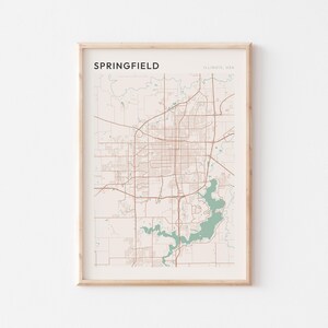 Puede incluir: Impresión enmarcada del mapa de Springfield, Illinois, EE. UU. El mapa presenta un diseño detallado de las calles en líneas marrones sobre un fondo beige. Un área verde representa un lago. La palabra "Springfield" está en la parte superior.