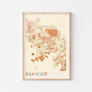 Könnte beinhalten: Gerahmter Kartendruck von Palm Desert, Kalifornien, USA. Die Karte zeigt einen detaillierten Grundriss der Stadt mit Straßen und Gebäuden in Beige- und Orangetönen. Die Worte "Palm Desert" sind unten in Braun gedruckt.