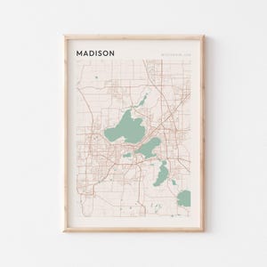 Puede incluir: Impresión enmarcada del mapa de Madison, Wisconsin, EE. UU. El mapa presenta un fondo beige con carreteras marrones y contornos de lagos verdes. La palabra "MADISON" está impresa en la parte superior, con "WISCONSIN, USA" debajo.
