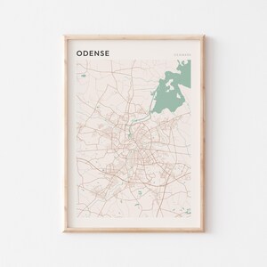 May include: Framed map print of Odense, Denmark, in a minimalist style. The map features a network of roads and streets in brown against a beige background. The word "ODENSE" is printed in black at the top left, with "DENMARK" on the top right.