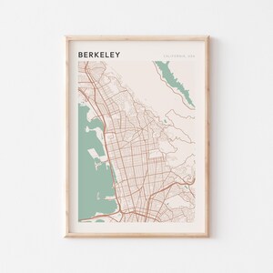 May include: Framed map print of Berkeley, California, USA. The map features a detailed street layout in brown against a beige background, with teal-colored water features. The word "BERKELEY" is printed at the top.