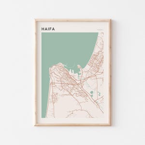 Puede incluir: Impresión enmarcada del mapa de Haifa, Israel. El mapa presenta un diseño de la ciudad en marrón claro sobre un fondo pálido, con una sección de color turquesa que representa el mar. La palabra "HAIFA" está impresa en la parte superior izquierda.