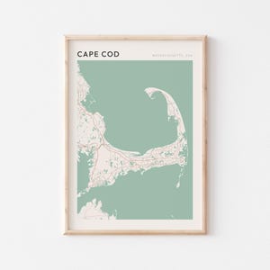 May include: A framed print showing a map of Cape Cod, Massachusetts, USA. The map has a minimalist design with a light green backdrop and white and red details. The text "CAPE COD" is at the top.