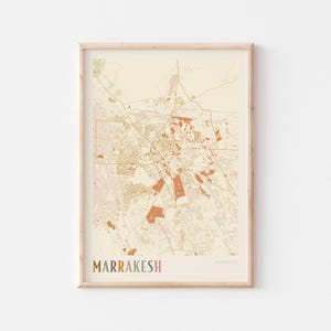 Puede incluir: Impresión enmarcada de un mapa de Marrakech, Marruecos, en una paleta de colores neutros. El mapa presenta calles y puntos de referencia detallados en tonos beige, marrón y naranja. La palabra "MARRAKESH" está impresa en la parte inferior en colores.
