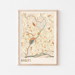 May include: A framed map print of Angers, France, in a neutral colour palette. The map features detailed streets, waterways, and landmarks in shades of beige, brown, and teal. The word "ANGERS" is printed at the bottom.