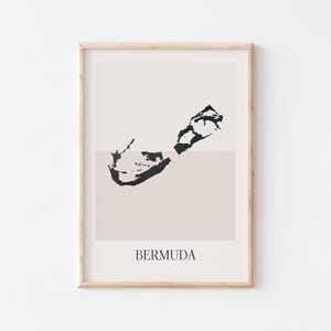 May include: A minimalist print of the island of Bermuda in black on a light beige background. The print is framed in a light wood frame. The text "BERMUDA" is printed below the island.