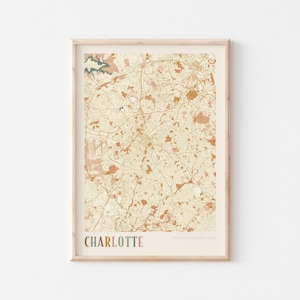 May include: A framed map print of Charlotte, North Carolina, USA. The map shows a detailed street layout in beige, brown, and orange hues. The word "CHARLOTTE" is printed in colourful letters at the bottom, with "NORTH CAROLINA, USA" below it.
