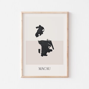 May include: A framed art print featuring a minimalist map of Macau in black against a neutral background. The word "MACAU" is printed in a clean font at the bottom. The artwork is encased in a light wood frame.