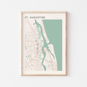 May include: Framed print of a map of St. Augustine, Florida, USA. The map has a light beige background with a green section on the right. The city's roads and waterways are in brown and the text "ST. AUGUSTINE" is at the top.