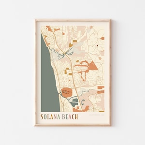 May include: A framed map print of Solana Beach, California, in a minimalist style. The map features a muted color palette of beige, orange, and green, with the city name at the bottom. The print is in a wooden frame.