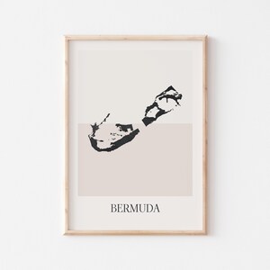 May include: A framed art print with a minimalist black and white illustration of Bermuda. The artwork has a neutral colour palette with a beige background and a light wood frame. The word "BERMUDA" is printed in a simple font.