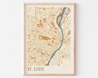 May include: A framed map print of St. Louis, Missouri, USA. The map features a detailed street layout in shades of beige, orange, and green, with the city's name at the bottom. The print is encased in a light-colored wooden frame.