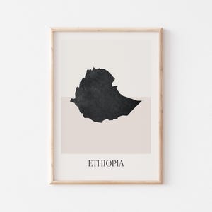 Puede incluir: Impresión artística enmarcada con un diseño minimalista del mapa de Etiopía en negro sobre un fondo beige y blanco. La palabra "ETHIOPIA" está impresa en una fuente sencilla en la parte inferior. La obra de arte está enmarcada en un marco de madera clara.