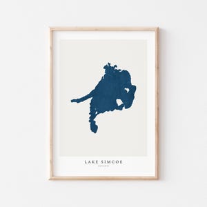 May include: A framed print of a blue silhouette of Lake Simcoe, Ontario. The print has a beige background and the lake's name and location are printed in black at the bottom.