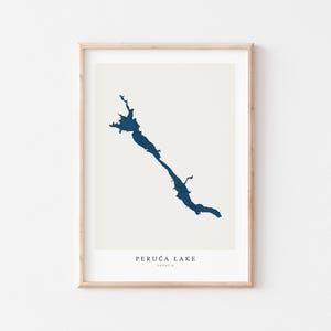 May include: A framed print featuring a minimalist map of Peruća Lake in Croatia. The lake's shape is rendered in a deep blue hue against a cream background. The text "PERUCA LAKE CROATIA" is printed in a simple font at the bottom.