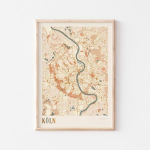 Puede incluir: Una impresión enmarcada del mapa de Colonia, Alemania, en una paleta de colores neutros. El mapa presenta una representación detallada del diseño de la ciudad, con un río prominente que la atraviesa. La palabra "KÖLN" está impresa en dorado en la parte inferior.