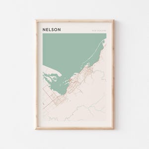 Puede incluir: Impresión artística enmarcada del mapa de Nelson, Nueva Zelanda, con el nombre de la ciudad en la parte superior izquierda. El mapa presenta un cuerpo de agua verde claro, una masa terrestre beige y carreteras rojas. El texto "NEW ZEALAND" está en la parte superior derecha.