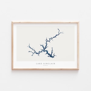 Può includere: Una stampa incorniciata di una mappa del lago Sinclair in Georgia. Il lago è delineato in blu scuro su uno sfondo beige chiaro. Il testo "LAKE SINCLAIR GEORGIA" è stampato sotto la mappa.