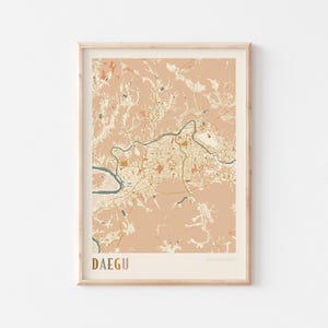 Op de afbeelding: Een ingelijste kaartprint van Daegu, Zuid-Korea, in een minimalistische stijl. De kaart toont een gedetailleerde plattegrond van de stad met een gedempte kleurenpalet van perzik, beige en bruine tinten. Het woord "DAEGU" staat onderaan in een schreefletter.