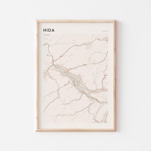 Puede incluir: Una impresión enmarcada del mapa de Hida, Japón. El mapa presenta una ilustración detallada del diseño de la ciudad, con carreteras y vías fluviales en tonos marrones, verdes y beige. La palabra "HIDA" está impresa en la parte superior izquierda, con "JAPAN" en la parte superior derecha.