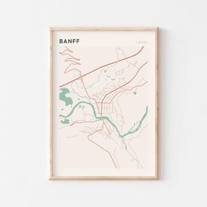 Peut inclure: Une impression encadrée d'une carte de Banff, au Canada, avec un design minimaliste. La carte utilise une palette de couleurs neutres avec des accents beiges, bruns et turquoise. Le nom de la ville est imprimé en gras, en police sans-serif en haut.