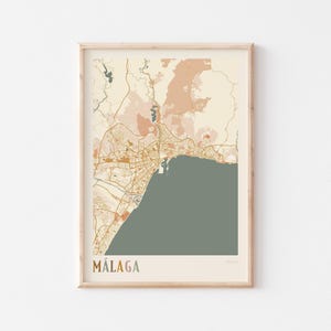 May include: A framed map print of Málaga, Spain, in a minimalist style. The map features a muted color palette of beige, orange, and green, with the city's name at the bottom. The print is encased in a light-colored wooden frame.