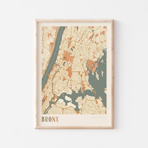 May include: A framed map print of the Bronx, New York, USA. The map features a muted color palette of beige, orange, and teal, with the word "BRONX" printed in a gold-colored font at the bottom. The map is encased in a light-colored wooden frame.
