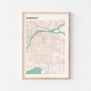 May include: Framed map print of Surrey, Canada, in a minimalist style. The map features brown roads and buildings, with teal-colored water features. The word "SURRREY" is printed at the top, with "CANADA" to the right.