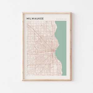May include: Framed map print of Milwaukee, Wisconsin, USA. The map features a detailed street grid in a warm brown hue against a light beige background. The city's outline is adjacent to a green section representing Lake Michigan.