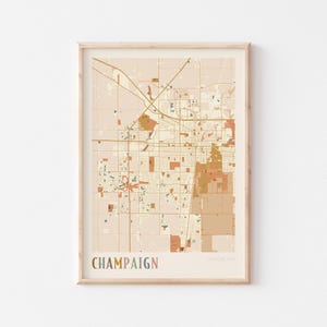 May include: Framed map print of Champaign, Illinois, USA, in a neutral color palette. The map features roads, buildings, and green spaces, with the city name in a colorful font at the bottom. The print is in a wooden frame.