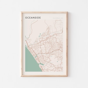 Könnte beinhalten: Eine gerahmte Karte von Oceanside, Kalifornien, USA. Die Karte ist in einem hellen Holzrahmen und zeigt die Straßen und Sehenswürdigkeiten der Stadt in Braun und Grün.