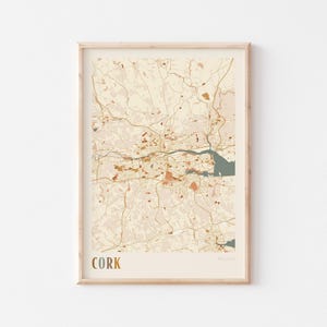 May include: A framed map of Cork, Ireland, with a beige background and brown and orange lines representing roads and streets. The city name "Cork" is printed in gold at the bottom left corner.
