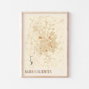 May include: A framed map print of Aguascalientes, Mexico, in a neutral color palette. The map details the city's layout with roads and buildings in shades of brown and orange against a cream background. The city name is printed in a multi-colored font.