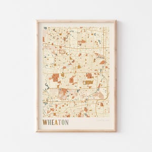 May include: Framed map print of Wheaton, Illinois, USA, in a neutral color palette. The map features a detailed street grid, with areas of orange, brown, and beige. The word "WHEATON" is printed in a muted color at the bottom.
