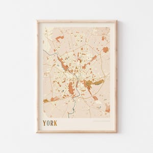 Puede incluir: Impresión enmarcada de un mapa de York, Reino Unido, en estilo minimalista. El mapa presenta un fondo beige con detalles marrones y naranjas, mostrando carreteras, edificios y zonas verdes. La palabra "YORK" está impresa en dorado en la parte inferior.
