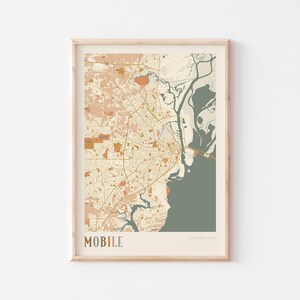 May include: Framed map print of Mobile, Alabama, USA, in a neutral color palette. The map features a detailed depiction of the city's layout, including roads, waterways, and green spaces. The word "MOBILE" is printed in a serif font at the bottom.