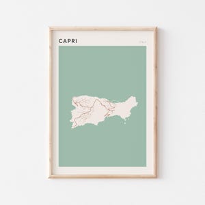 May include: Framed art print featuring a map of Capri, Italy. The map is in a light beige color, set against a muted green background. The word "CAPRI" is printed in black at the top, with "ITALY" in smaller text.