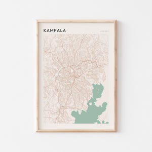 Könnte beinhalten: Gerahmter Kartendruck von Kampala, Uganda. Die Karte zeigt ein Netzwerk brauner Straßen und Wege auf beigem Hintergrund. In der unteren rechten Ecke befindet sich eine grüne Wasserfläche. Das Wort "Kampala" ist oben aufgedruckt.