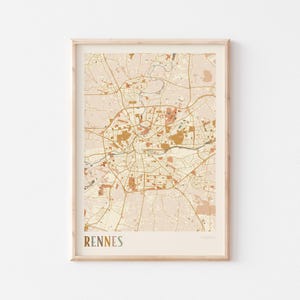 May include: A framed map print of Rennes, France, in a neutral color palette. The map features detailed streets, parks, and waterways in shades of beige, peach, and brown. The word "RENNES" is printed in a serif font at the bottom.