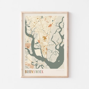 May include: A framed map print of Brunswick, Georgia, USA. The map features a detailed street layout in tan and orange hues, with a large river system in shades of green and gray. The word "Brunswick" is printed at the bottom.