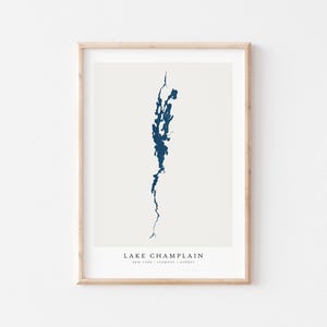 May include: A minimalist print of Lake Champlain, a body of water that borders New York, Vermont, and Quebec. The print is in a light beige colour with a dark blue outline of the lake.