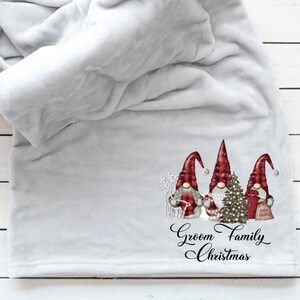May include: A light grey blanket featuring a Christmas gnome design. The gnomes have red hats and hold a Christmas tree and gifts. The text "Groom Family Christmas" is printed below the gnomes.