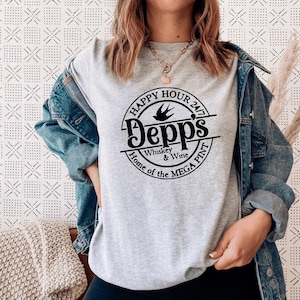 Op de afbeelding: Lichtgrijs t-shirt met een zwarte cirkelvormige afbeelding met de tekst "Happy Hour 24/7 Depps Whiskey & Wine Home of the MEGA PINT". Het shirt wordt gedragen.